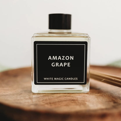 Square glass reed diffuser candles  bottle with a black label reading "AMAZON GRAPE" and "WHITE MAGIC CANDLES."